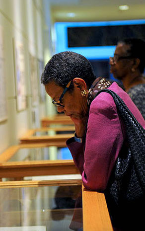 Photograph of woman with dark skin tone viewing exhibit display cases