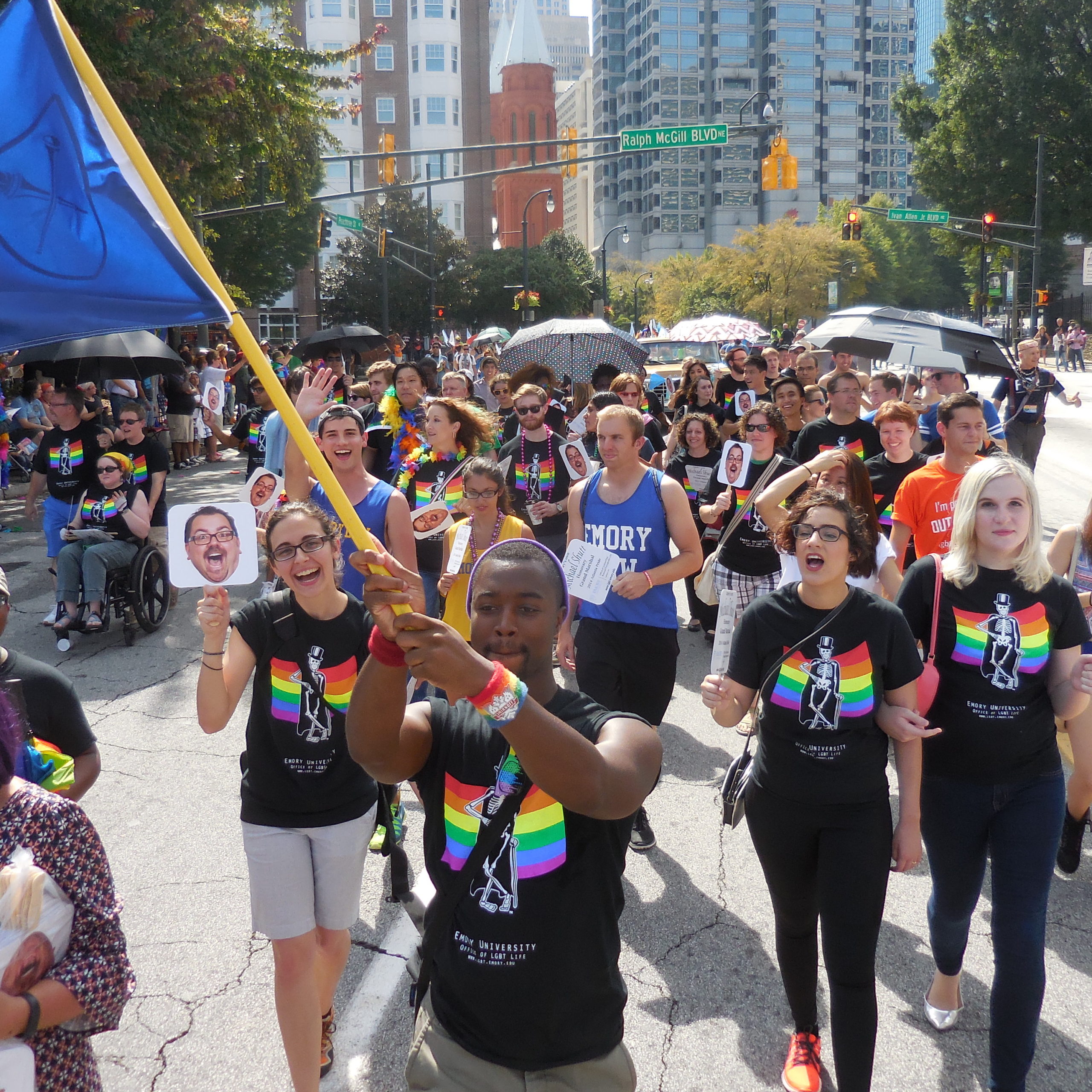 Crowd marching in a pride parade and wearing black shirts with an image of a skeleton in front of a rainbow