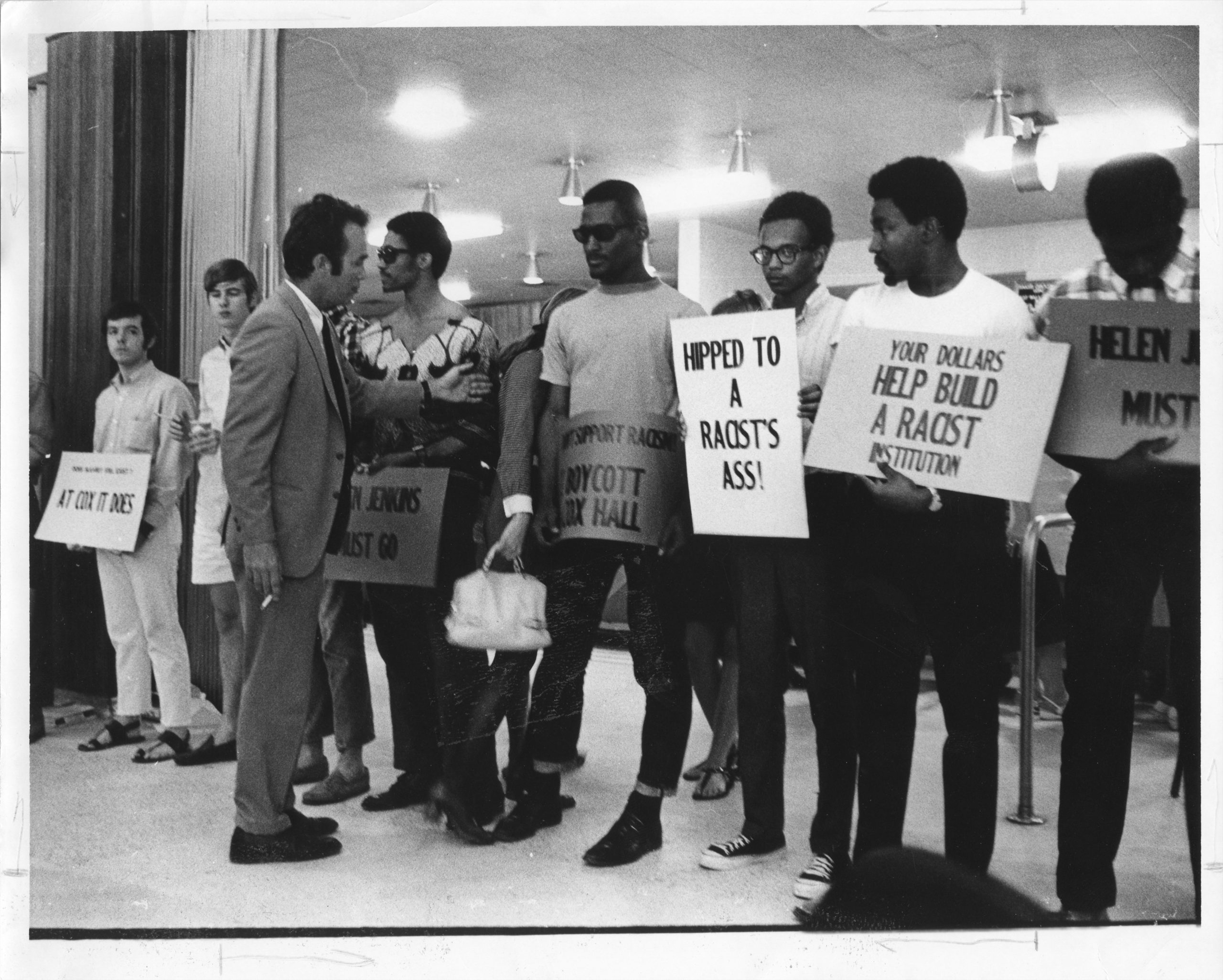 Photo of student protestors holding signs, including "your dollars helped build a racist institution"