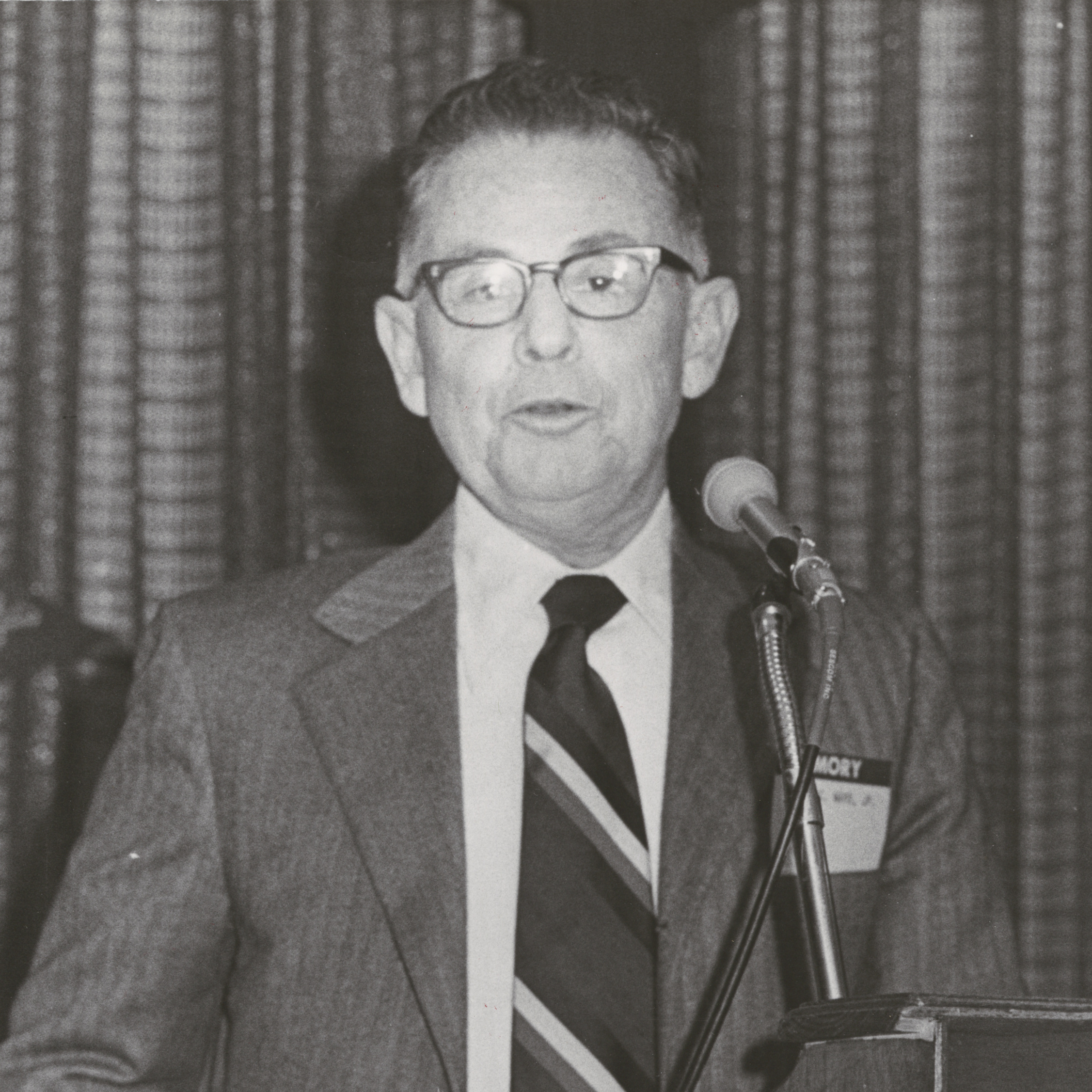 Judson C. Ward, man in glasses and suit, speaking into microphone at podium