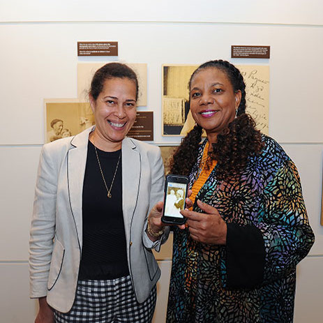 Photograph of woman with medium skin tone and woman with medium-dark skin tone holding photograph on phone
