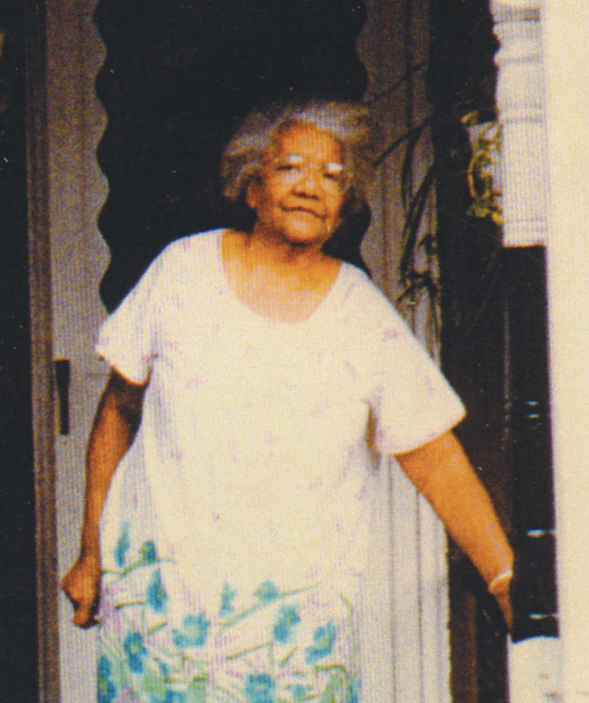 Photograph of older woman with medium-dark skin tone standing on a porch