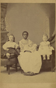 Photograph of two children with light skin tone seated next to child with dark skin tone holding infant with light skin tone