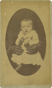 Photograph of infant with light skin tone being held by hands with dark skin tone