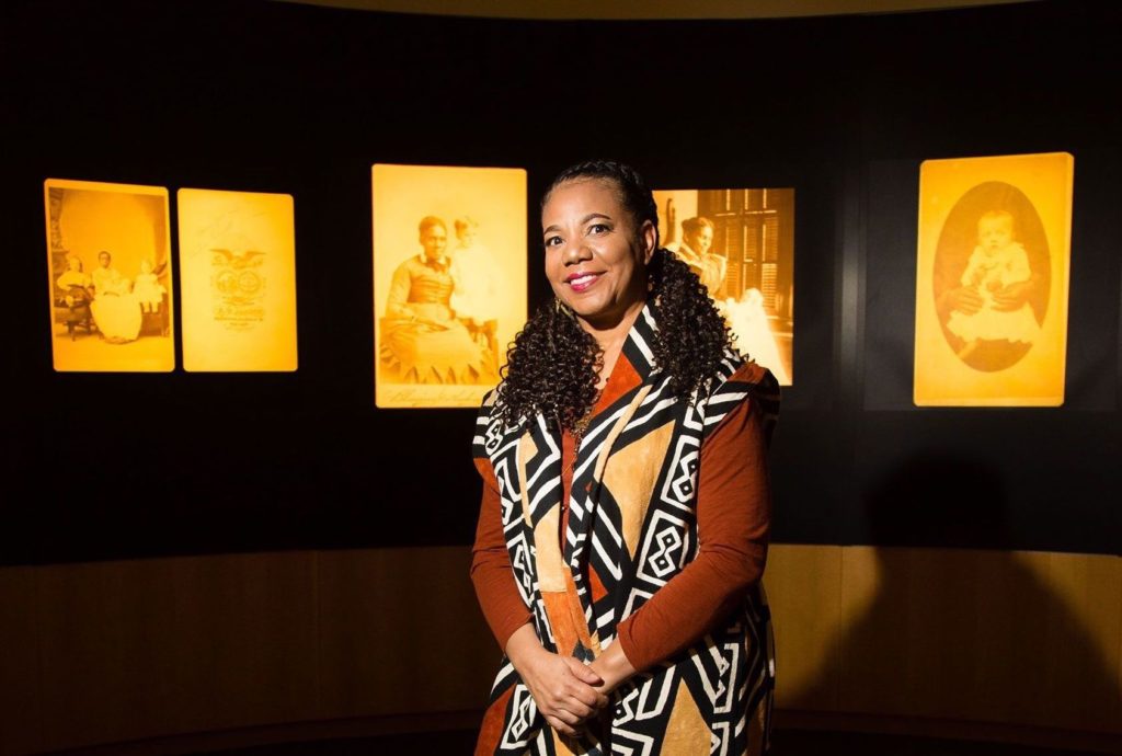 Photograph of woman with medium-dark skin posing with archival photographs