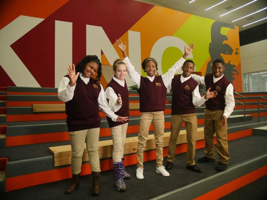 Five students in matching uniforms pose in front of a colorful mural of Martin Luther King Jr.