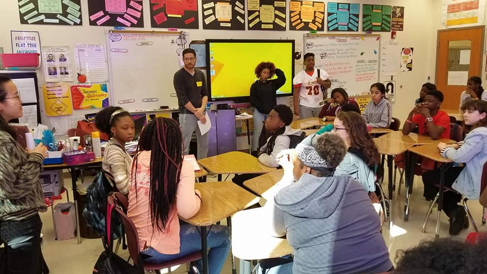 Classroom with students seated at desks and wall of posters and whiteboards