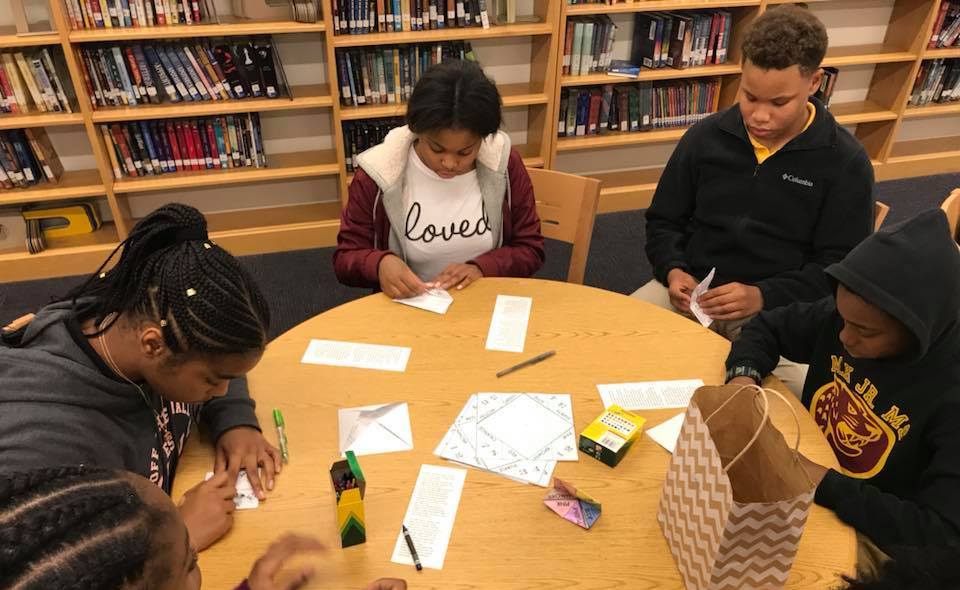 Five students creating paper fortune tellers in a library