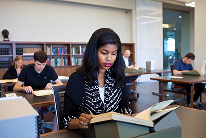 People reading at rows of large desks in front of bookshelves in Rose Library reading room